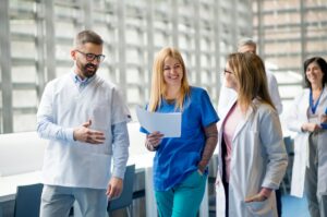 Group of healthcare professionals in a bright hospital hallway, smiling and walking together, discussing a document.