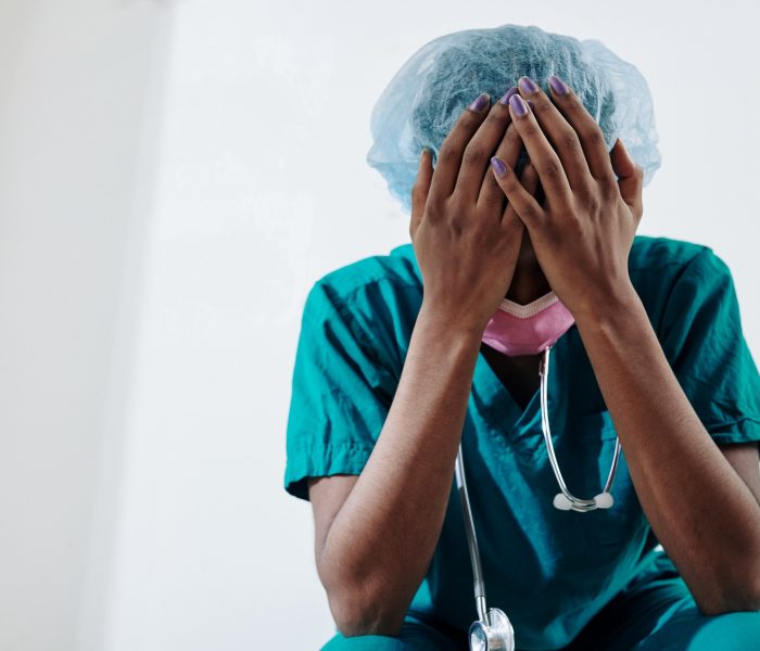 Crying nurse covering her face with hands, she is tired of working extra hours and seeing suffering and dying people